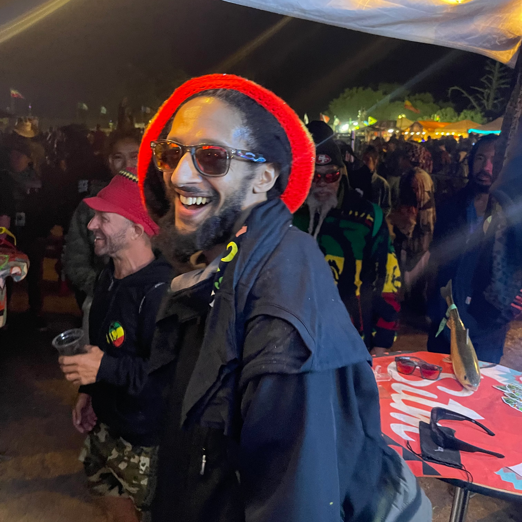 Man with red beanie and sunglasses smiling at a music festival.